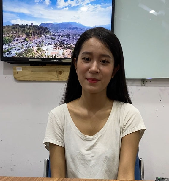 A young woman sitting at a desk in front of a TV, her attention grabbed by the screen.