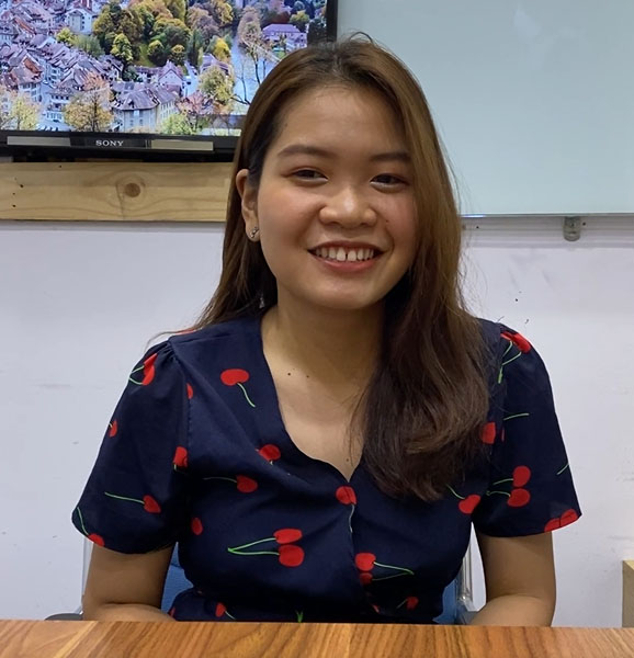 A smiling woman sitting at a desk in front of a tv, providing Kuala Lumpur escort services.
