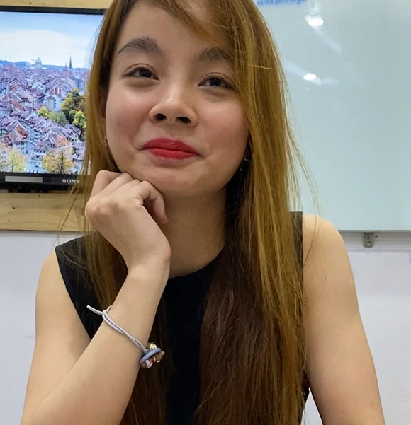 Asian woman sitting in front of a computer, contemplating with her hand on her chin.